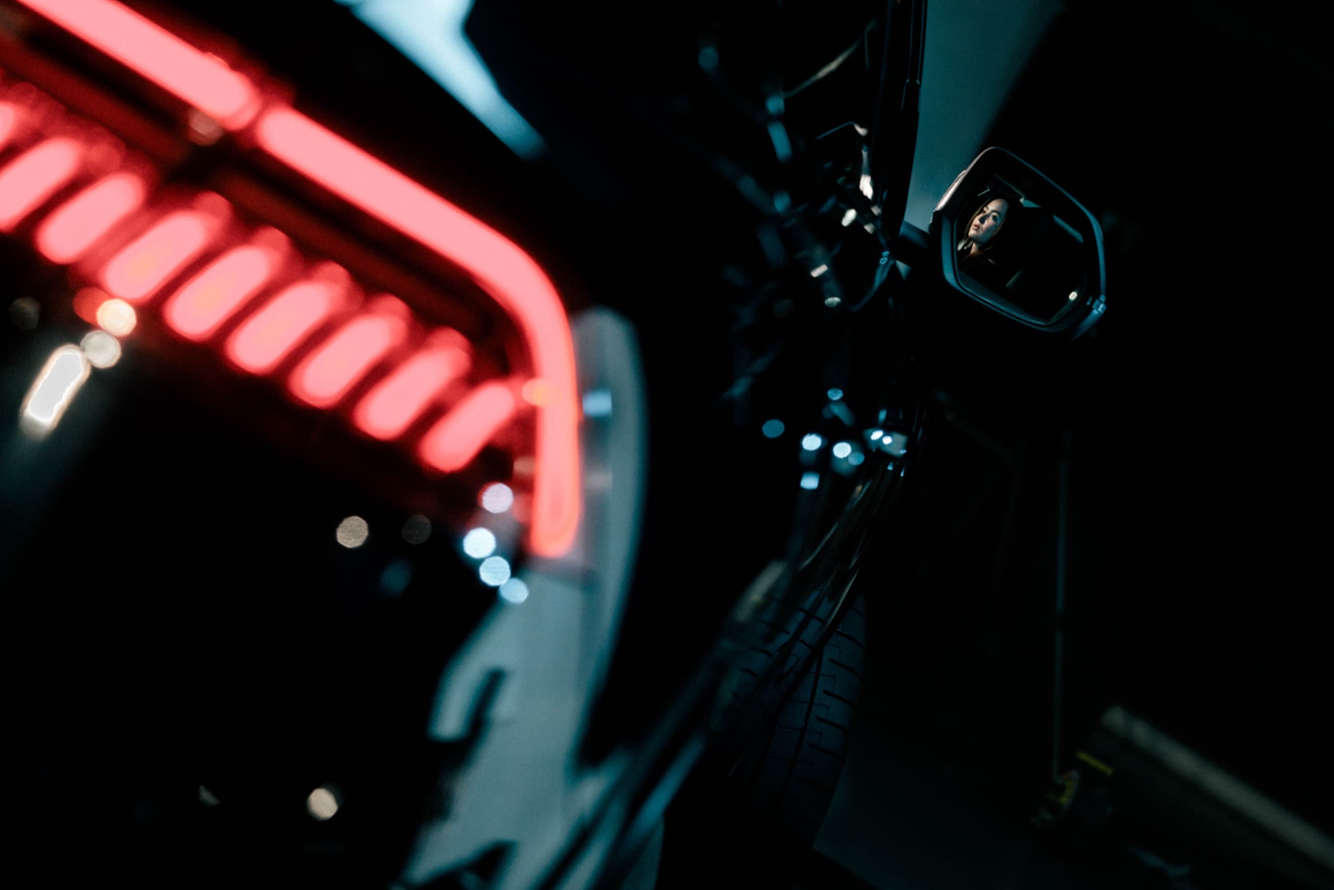 Piloto trasero rojo en primer plano y rostro reflejado en el retrovisor
